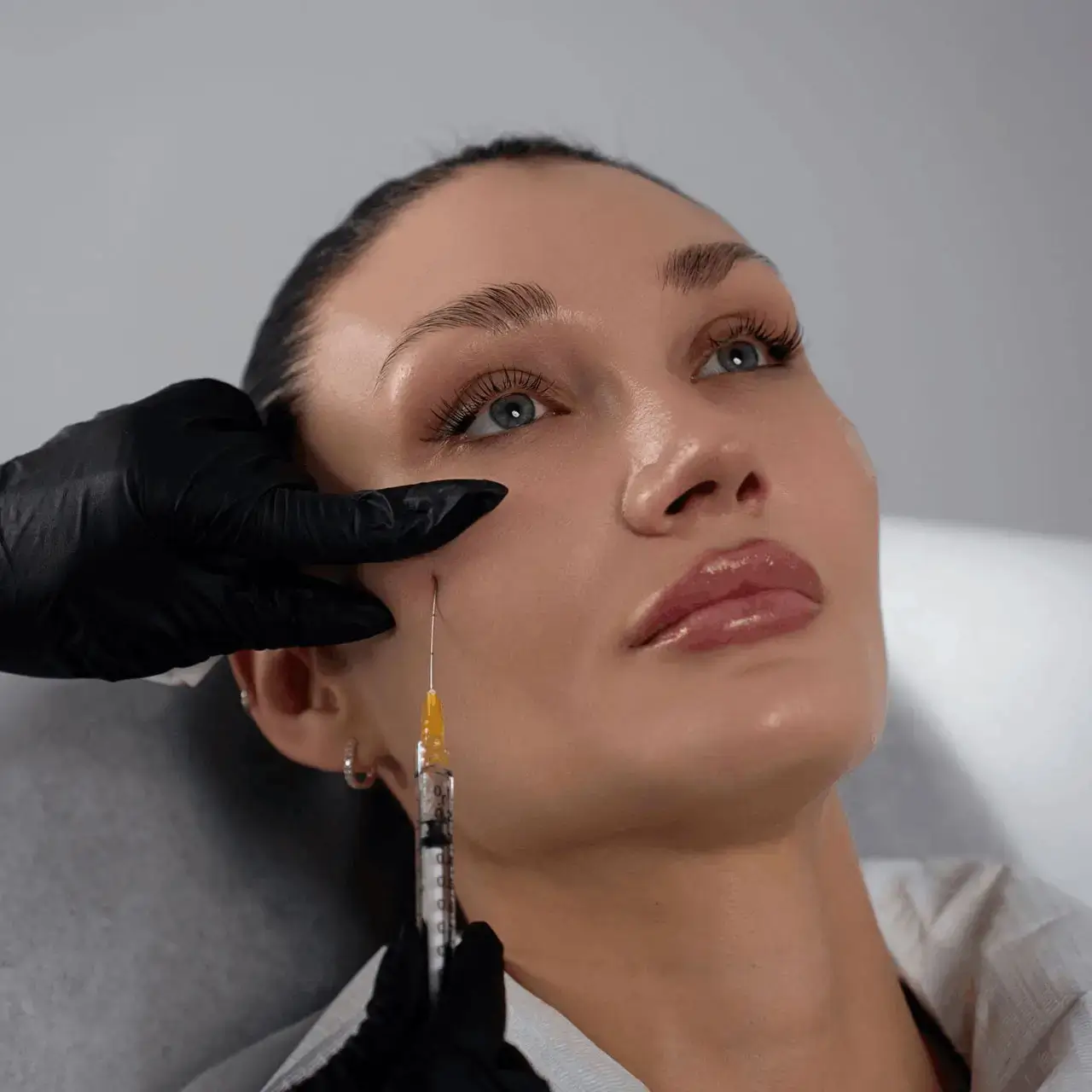 Gloved injector giving a fine-needle injection near the temple and upper cheek of a reclining client
